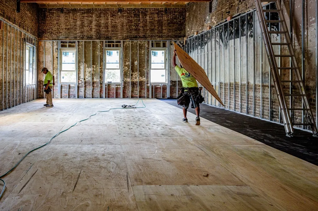 Gutted room with exposed framing and a worker carrying lumber